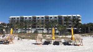 Un hôtel en bord de mer doté de nombreux balcons, de chaises de plage et de parasols.