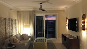 Un salon comprenant un canapé, une table basse, un téléviseur fixé au mur et un ventilateur de plafond.