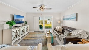 A living room with a TV, sofa, and a view through a glass door to the outdoors.