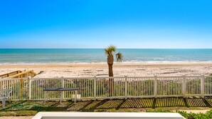 A beach view with a white fence, a palm tree, and a wooden deck.