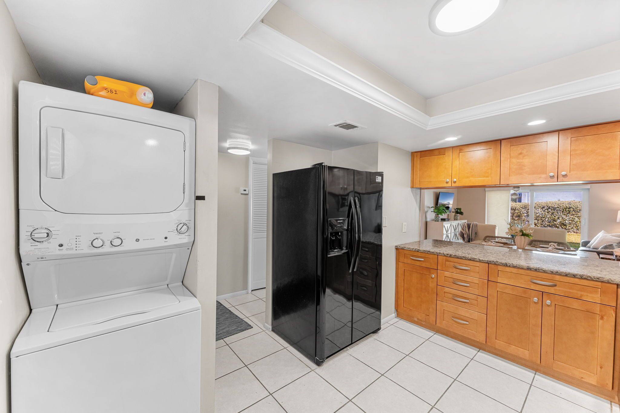 A kitchen with a washing machine, a black refrigerator, wooden cabinets, and a countertop.