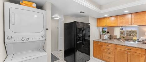 A kitchen with a washing machine, a black refrigerator, wooden cabinets, and a countertop.