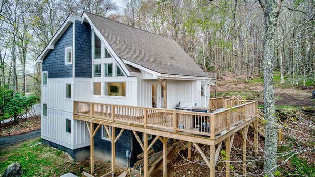 A two-story cabin with a deck, surrounded by trees. - Elevation Escape - Beech Mtn home with game room, outdoor space (Beech Mountain)