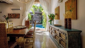 A dining area with a wooden table, chairs, a chandelier, and a view of an outdoor pool.