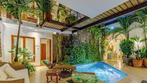 A spacious indoor area with a pool, wicker furniture, and lush greenery.