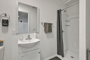 A modern bathroom with a white sink, mirror, and shower area. - The Nest At Columbia City (Seattle)