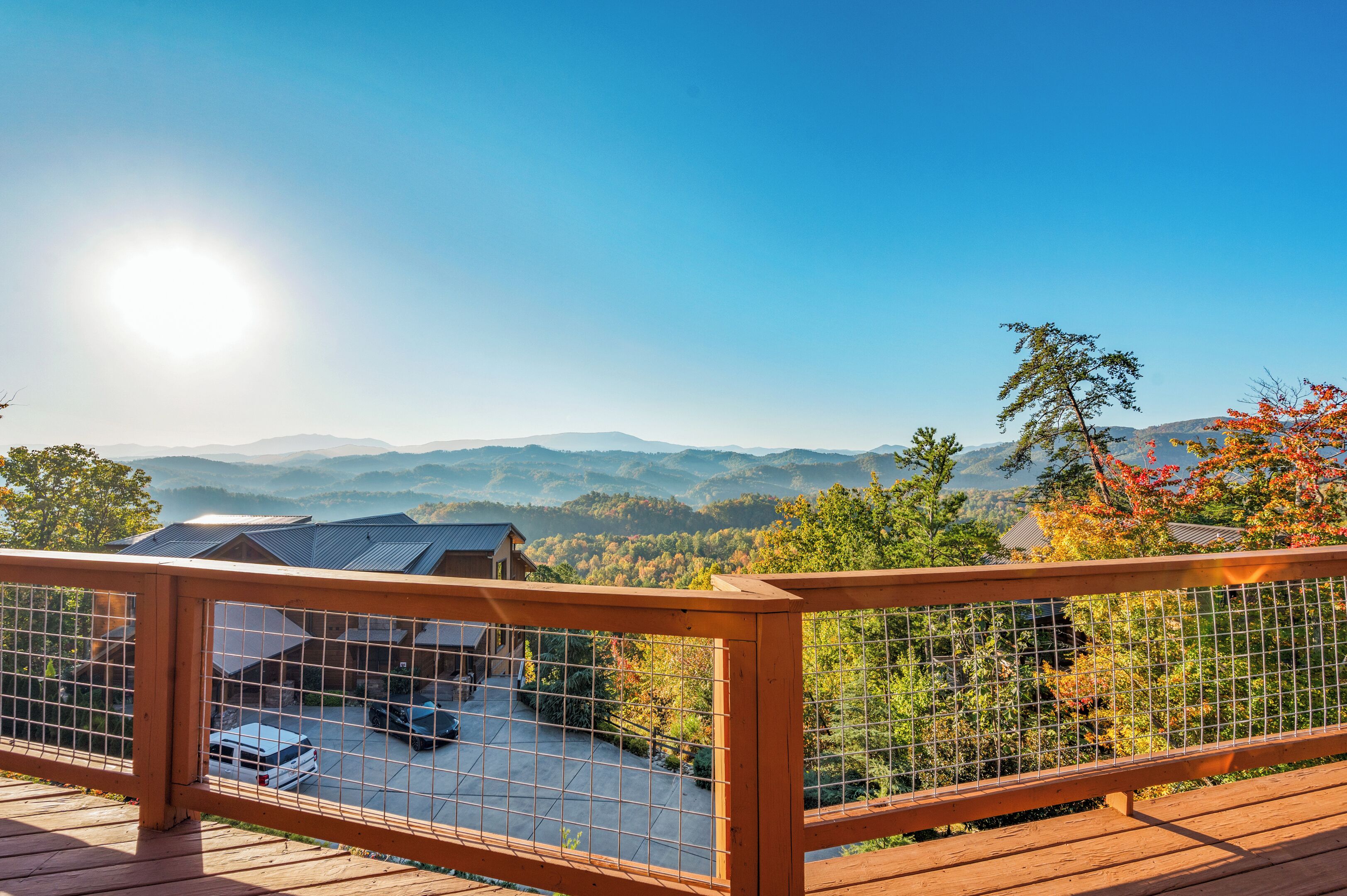 Une terrasse en bois avec une rambarde en métal, d’où l’on peut admirer un paysage montagneux aux couleurs automnales.