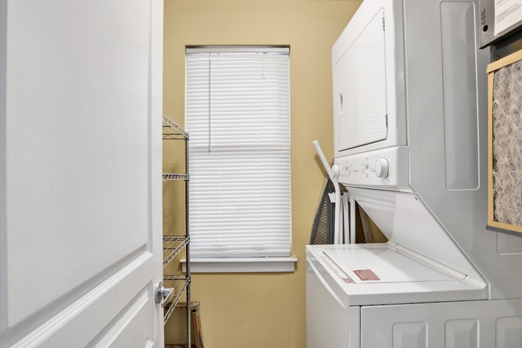 A laundry room with a washing machine, dryer, and a window with blinds.