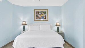 A bedroom with a bed, two bedside lamps, a ceiling fan, and a framed artwork on the wall. - Silver Beach 506 | Pet Friendly, Direct Gulf Front, Great Location!! (Orange Beach)