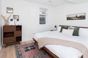 A bedroom with a bed, a bedside table, a lamp, a window, and a wooden dresser. - Cabin Near Old Man's Cave · Sleeps 6 · Hot Tub (Laurelville)