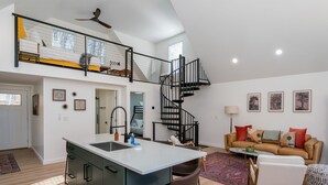 Een ruime woonkamer met een moderne keuken, een eethoek en een trap naar een hoger gelegen verdieping.