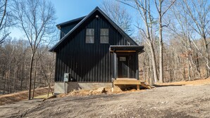 Een rustieke houten chalet met een steile puntige dak, een veranda en een kleine trap naar de ingang.