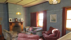 Ein traditionell eingerichtetes Wohnzimmer mit Kamin, mehreren Sesseln, einem Tisch und einer Chandelier.