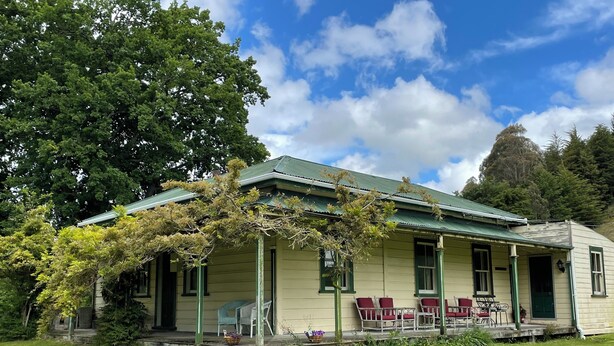 Ein Haus mit Veranda, grünem Dach und einem Baum davor.