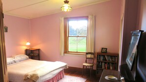Ein Schlafzimmer mit einem Bett, einem Sessel, einem Bücherregal, einem Fernseher und einem Fenster.