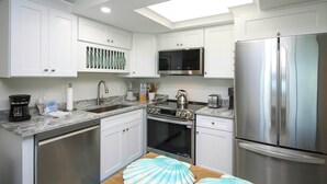 Una cocina moderna con armarios blancos, electrodomésticos de acero inoxidable, lavavajillas y microondas.