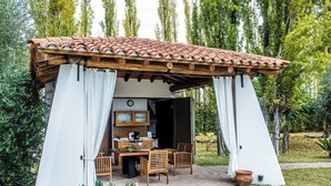 Une cuisine extérieure rustique, dotée d’un toit en tuiles, de meubles en bois et d’une horloge au mur.