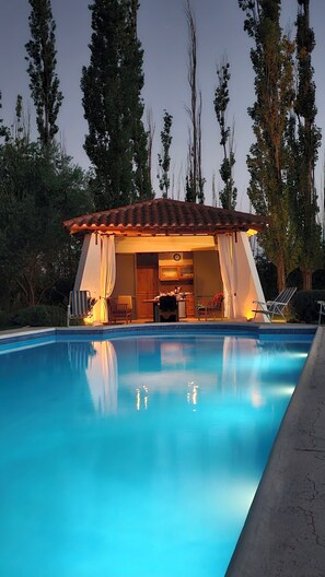 Un espace aménagé au bord de la piscine, comprenant un coin salon couvert, une table à manger et des chaises.