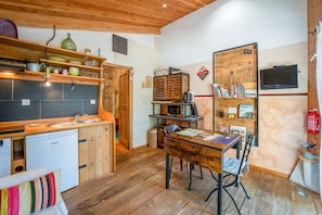 A compact kitchen with a refrigerator, sink, and wooden cabinets. There's a dining table with chairs and a small bookshelf. - Holiday Home 'La Poulido' with Private Terrace, Private Garden and Wi-Fi (Bedoin)
