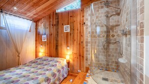 Een houten kamer met een bed, een douche met stenen tegels en een raam met gordijnen.