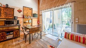 Een gezellige kamer met een houten tafel, stoelen, een bank, een televisie en een schuifdeur naar een buitenruimte.