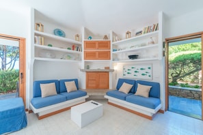 Un salon avec deux canapés bleus, une table basse blanche et des étagères intégrées où sont disposés des livres et des objets décoratifs.