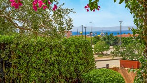 A view of a coastal area with a clear sky, a street with parked cars, and a body of water in the distance. - Apartment 'Mazzini' with Sea View, Wi-Fi, and Air Conditioning (Golfo Aranci)