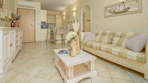 A living room with a sofa, coffee table, and a dining area with chairs and a table. - Apartment 'Mazzini' with Sea View, Wi-Fi, and Air Conditioning (Golfo Aranci)
