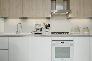 Una cocina moderna con armarios blancos, una campana extractora de acero inoxidable, un horno empotrado y una cafetera.