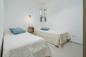 Un dormitorio con dos camas, una mesita de noche, una lámpara y una ventana.