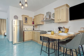 Una cocina moderna con armarios de madera, un refrigerador de acero inoxidable y una zona de comedor con una mesa de madera y taburetes de bar.