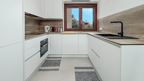 A modern kitchen with white cabinets, a wooden backsplash, a window with a view, and a black faucet.