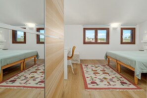A mirrored room with two beds, a chair, a rug, and windows with a view.