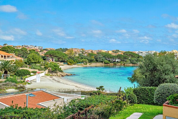 A coastal view with a beach, residential buildings, and greenery.