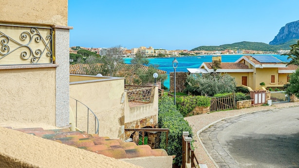 A coastal residential area with a clear view of the sea, a paved street, and a building with a balcony.