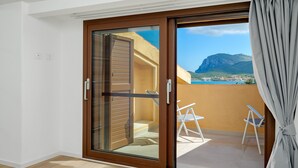 A room with a sliding glass door leading to a balcony with a view of a mountain and sea.