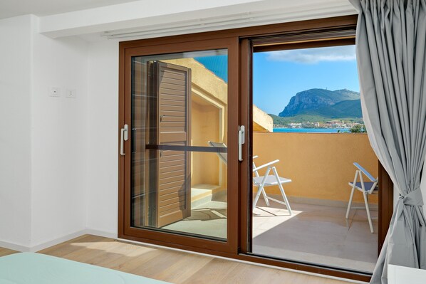 A room with a sliding glass door leading to a balcony with a view of a mountain and sea.
