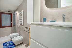 A modern bathroom with a glass shower enclosure, a white sink, and a bidet.