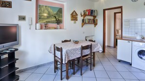 A dining area with a table, chairs, a television, and a kitchen with a washing machine. - Apartment 'Tramonto' with Private Terrace, Wi-Fi and Air Conditioning (Capoliveri)