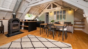 Habitación tipo ático con chimenea, mesa de comedor de madera, sillas y zona de cocina.