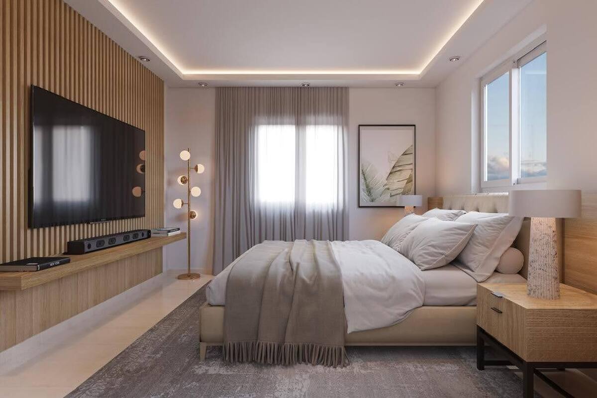 Un dormitorio moderno con un televisor grande, una mesita de noche con lámpara, una cama con manta color beige y un ventanal amplio.