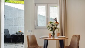 A dining area with a round table, two chairs, a vase with flowers, and a window with curtains.