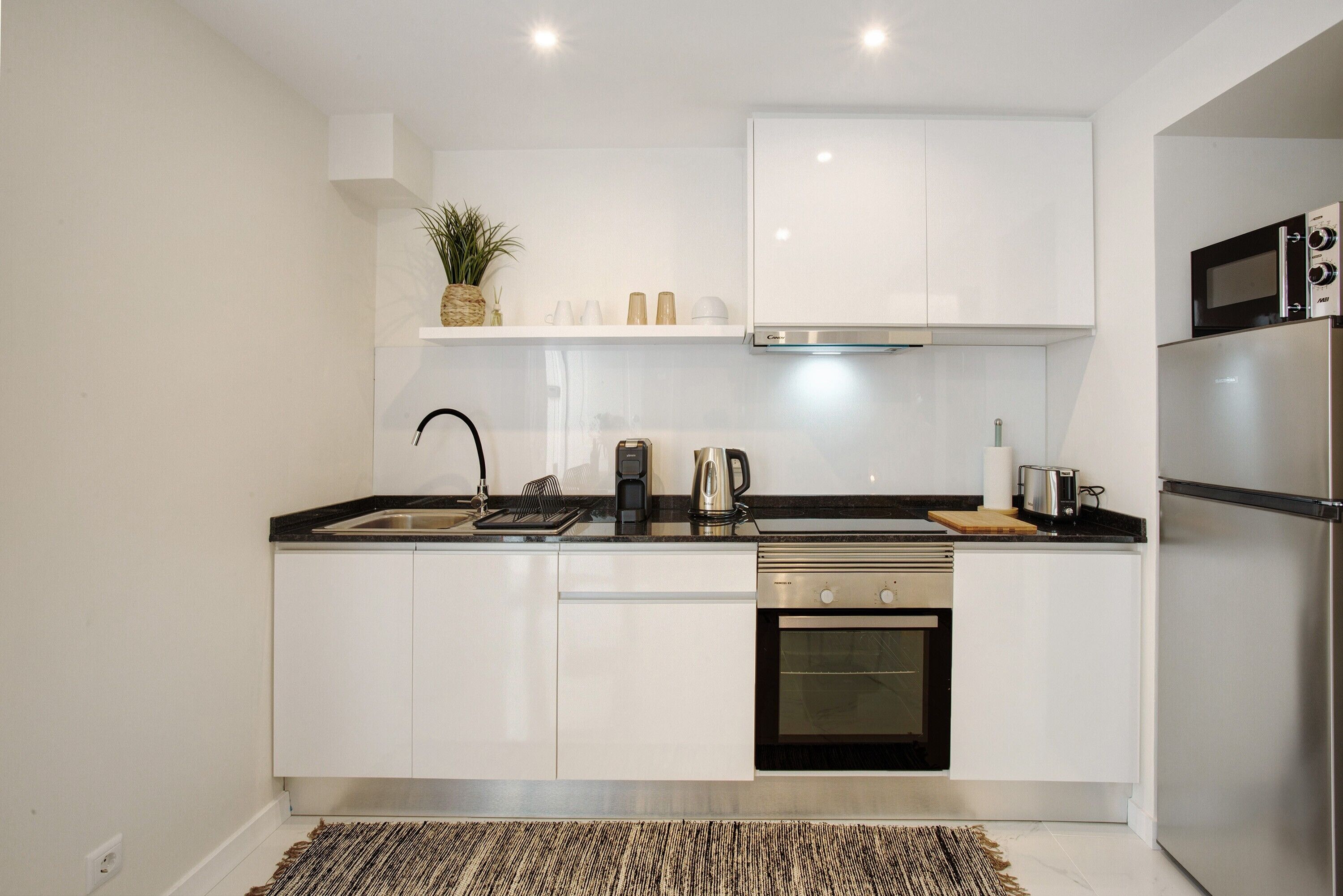 Una cocina moderna con armarios blancos, estufa de acero inoxidable, horno empotrado y microondas.