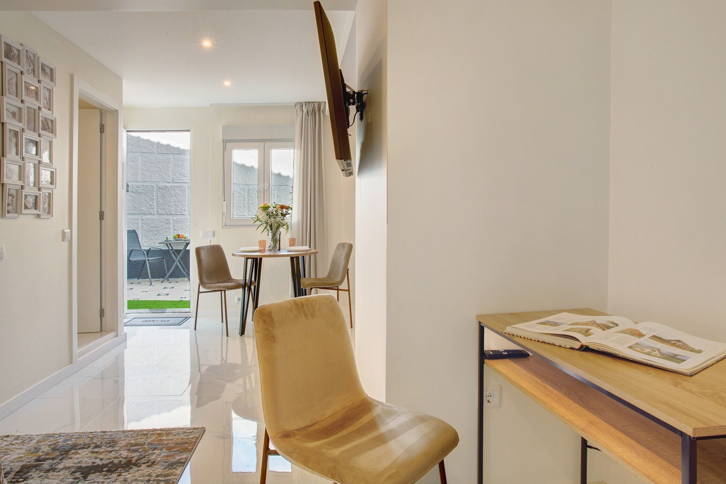 Una sala de estar moderna con un sofá, una mesa de comedor con sillas, un televisor montado en la pared y vistas al exterior.