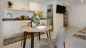 A modern kitchen with white cabinets, a dining table with a vase of flowers, and a flat-screen TV mounted on the wall.