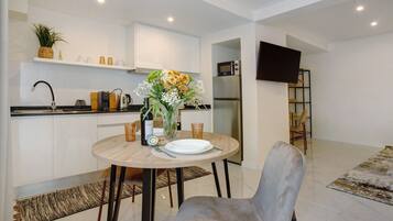 A modern kitchen with white cabinets, a dining table with a vase of flowers, and a flat-screen TV mounted on the wall.