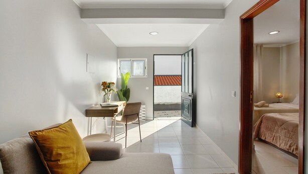 A modern living room with a sofa, a dining area with a table and chairs, and a view of a balcony with a red-tiled roof.
