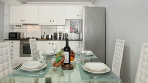 A modern kitchen with white cabinets, a glass dining table, and a refrigerator.