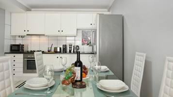 Een moderne keuken met witte kasten, een glazen eettafel en een koelkast.