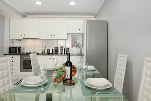 Een moderne keuken met witte kasten, een glazen eettafel en een koelkast.